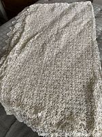 Full view of the cream crocheted tablecloth showing overall pattern and condition with minor wrinkles and stains.