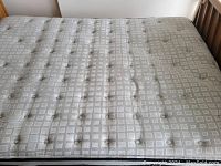 Close-up of mattress surface showing light grey fabric with button tufting.