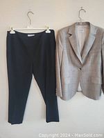 Two pieces of women's clothing hanging on a wall, showing a beige checkered blazer jacket and black pants.