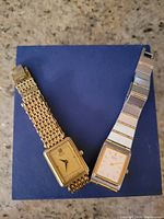 Two vintage Seiko ladies watches on a blue surface, showing both gold and silver tone with rectangular faces.