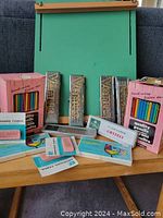 Wooden green artist easel, sets of Smilin' Joe colored pencils, multiple packs of Eberhard Faber erasers on a table.