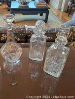 Photo of three crystal decanters with detailed etchings on table showing shapes and stoppers
