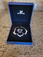 Melina pin brooch in black velvet-lined blue Swarovski box, showing flower shape with central blue crystal and clear crystals along petals.