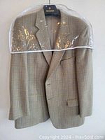 Full front view of the camel-colored plaid blazer on a hanger with a plastic cover over the shoulders.