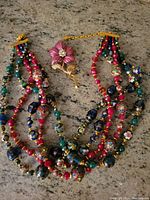 Full view of the Millefiori multi-strand glass bead necklace and enameled flower brooch on a granite surface.