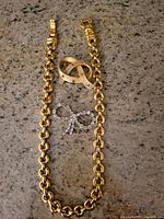 Photo showing the gold tone chain necklace laid flat with two bow-shaped brooches positioned inside the necklace loop on a granite surface.
