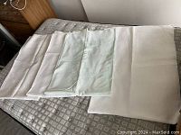 Five white or off-white tablecloths spread out partially, showcasing different sizes and subtle patterns with some minor visible staining.