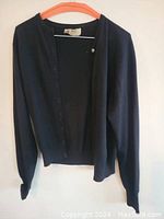 Front view of black Pringle of Scotland cashmere sweater hung on an orange hanger, button-up style, long sleeves