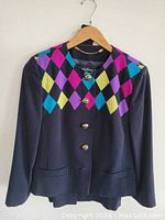 Front view of navy blazer with colorful diamond pattern and gold buttons on hanger