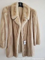 Front view of vintage blonde mink coat hanging on hanger against plain background