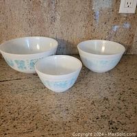 Front view of three vintage Pyrex Butterprint Amish mixing bowls in descending sizes with blue pattern on white glass