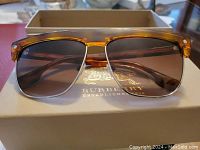 Front view of Burberry sunglasses showing tortoiseshell upper frame and metal lower frame with brown gradient lenses on Burberry box.
