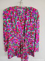 Full view of vintage Saint Laurent floral blouse with vibrant pink, red, purple floral pattern and green leaves, long sleeves, V-neck and front tie knot detail.