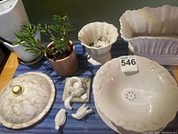 Wide scalloped planter, round scalloped planter, berry drainage bowl and platter, small marble birdbath, three white and pale pink planters arranged on blue cloth surface.