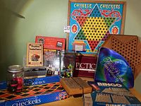 Photo shows the entire 20th Century Classic Games lot including Chinese Checkers board, Checkers sets, Bingo game, jar of marbles, Pictionary box, and Trivial Pursuit box arranged on a table.