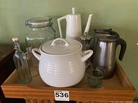 Photo showing all items on wooden tray including two stove top espresso makers, white teapot, soup tureen or cookie jar, glass pepper mill, and various glass storage containers and votive holder.