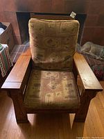 Front view of oak Craftsman style chair with patterned cushions, showing wood armrests and cushions with some wear.
