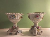 Pair of German floral ceramic vases shown from front with cutout flared rim, ceramic flower reliefs, and base with scroll design.