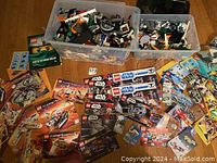 Photo showing two large plastic bins with mixed Lego pieces and many colorful instruction manuals spread around them, featuring multiple Lego themes.
