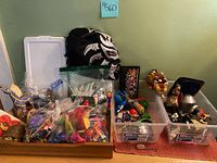 Wide shot of various kid's toys and accessories including figurines, wrestling mask, plush, and small toys in bins.