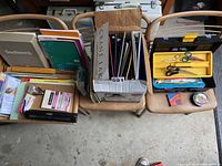 Wide shot showing boxes of binders, notebooks, and paper with office supplies on folding chairs
