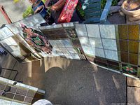Photo showing six stained glass panels arranged outdoors revealing overall design, colors, and general condition of multiple panels including centerpiece.