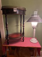 Photo of two-level wooden bar table with decorative details and creamy colonial style lamp placed on a red checked cloth surface against a green wall.