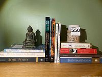 Books lined up side by side with meditating Buddha statue and ceramic mug on a green background.