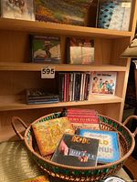 Woven basket filled with assorted CDs in cases, placed in front of wooden CD shelf. Visible CDs include Born to Swing, AC/DC, and others. Shelf holds additional CDs including Swing Era and One Direction albums.