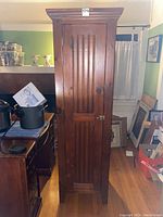 Closed view of the tall knotty pine cabinet showing the single door with vertical groove detailing and metal latch at front