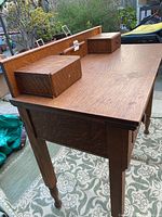 Angled side view of the tiger oak writers desk showing the wood grain, tapered legs, and two small top drawers with a pen storage channel.