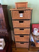 Front view of wicker storage tower with five drawers, wooden box on top, displaying overall condition and proportions.
