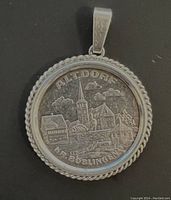 Front view of the silver pendant showing detailed Altdorf village scene and twisted rope border.