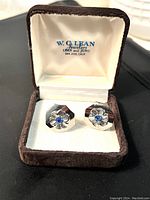 Pair of silver tone Art Deco cuff links with blue crystal centers displayed inside a brown velvet jewelry box marked W.G. Lean Jewelers, San Jose, Calif.