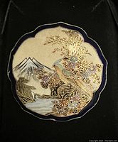 Front view of antique Japanese Satsuma porcelain brooch showing detailed hand-painted bird, flowers, mountain, and water scene with gold gilding.