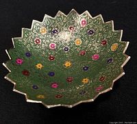 Image showing front and angled view of copper bronze dish with colorful floral design on green background and scalloped edges.