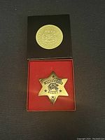 Photo of the vintage Wells Fargo Agent's star pin in black presentation box with red lining, showing the star shape with lettering and coach image.