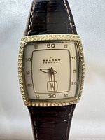 Front view of Skagen women's gold tone watch showing square face with pave crystal bezel and brown leather strap.