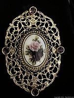 Front angle view of vintage brooch with gold-tone filigree, enamel floral centerpiece and amethyst rhinestones.