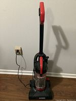 Photo of upright vacuum cleaner plugged into wall outlet showing overall condition and design