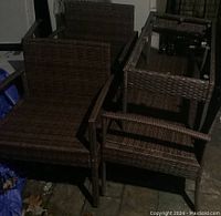 Overview of two brown wicker chairs and one bench stacked one on top of the other indoors, showing the seating surfaces and armrests.