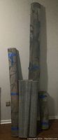 Four rolled carpets, three patterned and one solid gray roll, secured with blue tape.