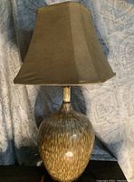 Full view of the ceramic lamp with brown fabric shade, showing color and shape details.