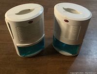 Two white and blue small indoor dehumidifiers placed side by side, showing front and top handle design.