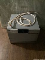 Front view of Danby countertop dishwasher with coiled water connection hose and faucet adapter on top