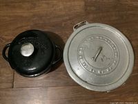 Black enameled Dutch oven and large silver metal Dutch oven with lids view from above on a wood floor
