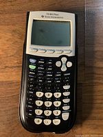 Front view of black and white Texas Instruments TI-84 Plus calculator showing screen and keypad.