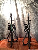 Two tall iron table lamps with ornate scrollwork bases, illuminated, against a light background.