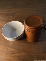 Five white ceramic Toy Story themed bowls stacked beside brown ceramic mason jar with metal latch lid.