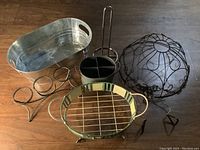Overview of four metal baskets and organizer including the oval metal basket on stand, black organizer, wire basket, and small painted basket.